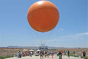 A big orange air balloon is about to take off while crowd watches