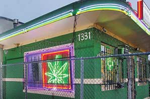 A medical marijuana dispensary shop with neon sign and secured by wired fence.
