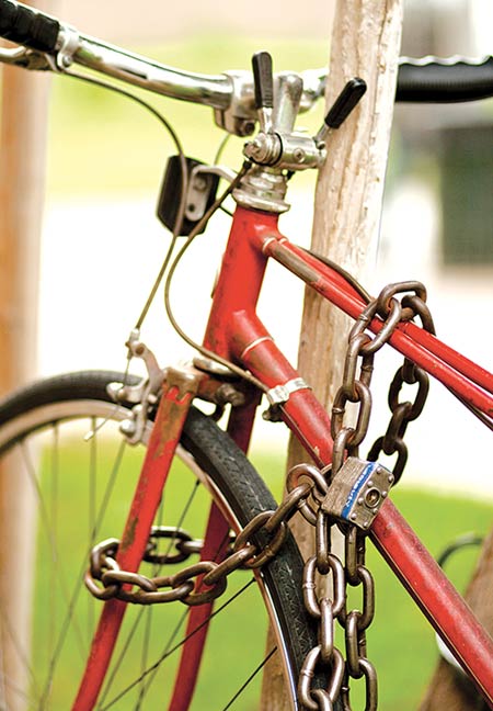 A red/silver/black bicycle with thick metal chain tied to a metal poll.