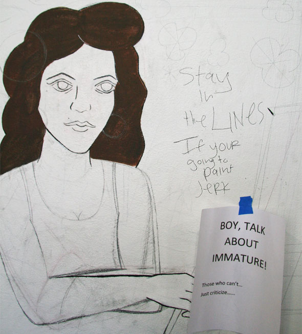 Graffiti of writing next to an art drawing of a women with long think hair reading Stay-in-the-LINES-If-your-going-to-paint-JeRK. Next to the graffiti is a printed note taped reading BOY,-TALK-ABOUT-IMMATURE!