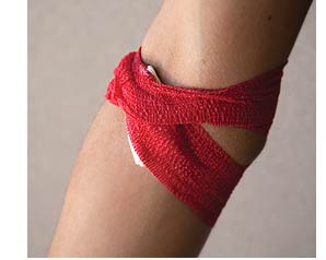An elbow with white gauze strapped with thick red elastic band.