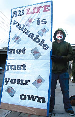 Juan Lerma wearing a hooded dark-green sweater with a white breathing mask over his mouth with the word LIFE in red print.