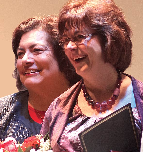 SAC President Erlinda Martinez and Math Professor and Distinguish Faculty Award winner Lynn Marecek smiling and holding flowers and their awards on the stage after they were presented with their respective awards.
