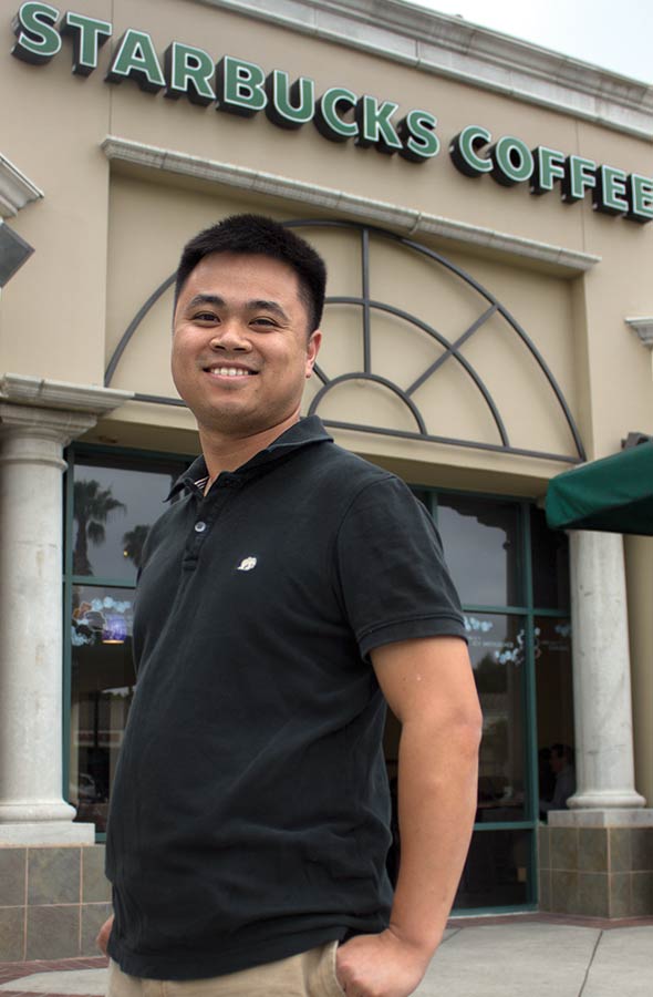 Chris Nyuyen wearing Starbuck's dark green collar shirt, standing and smiling in front of a Starbuck's Coffee. 