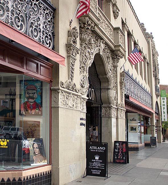Front of the Santora Building with two American flags waging. Several stores beside Santora Building have exclusive sculptured ceramic pattern on the top of the store fronts.