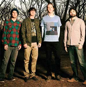 The Animal Collective foursome band members stand in front of the wood with tall leafless trees.